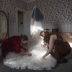 Bride gets help into dress from mother and sister.